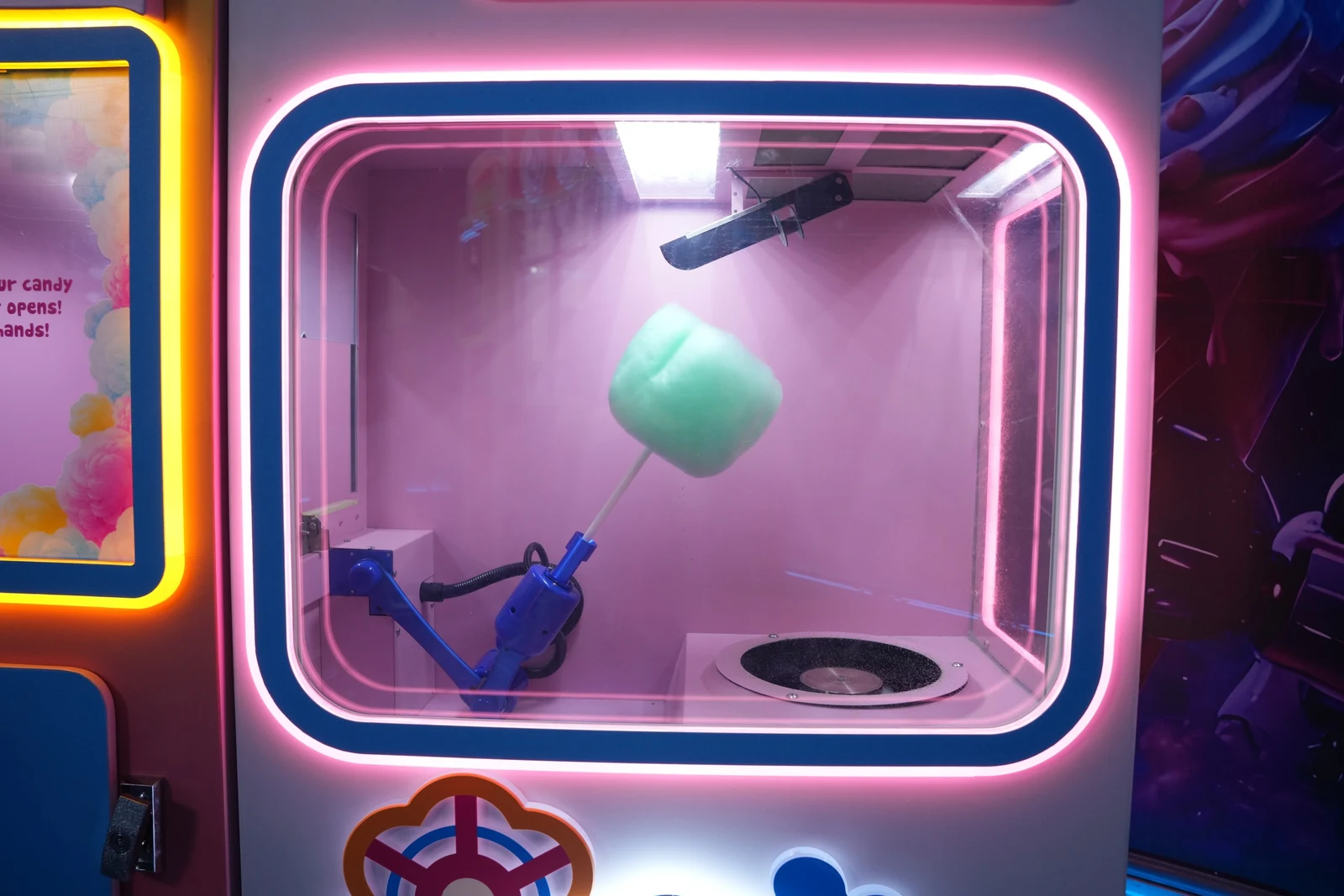 Robotic arm holding a fresh cotton candy inside the machine's neon-lit chamber