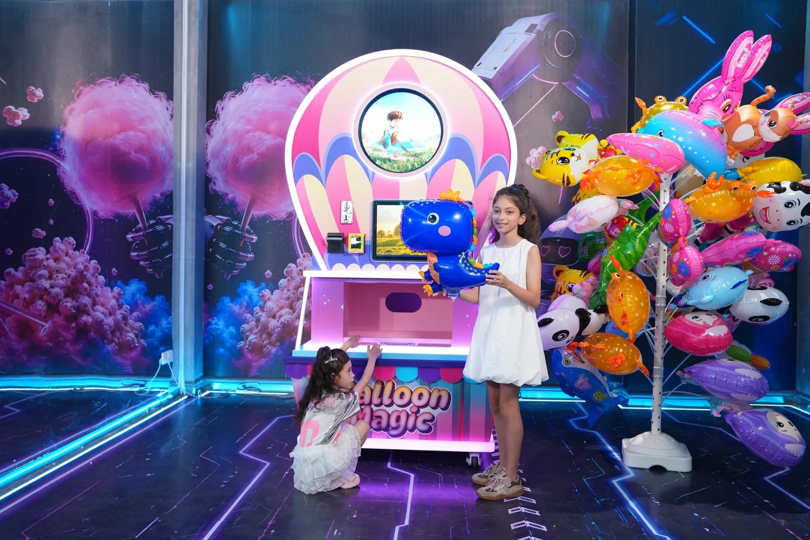 Two girls holding foil balloons next to the Futureino Balloon Magic machine