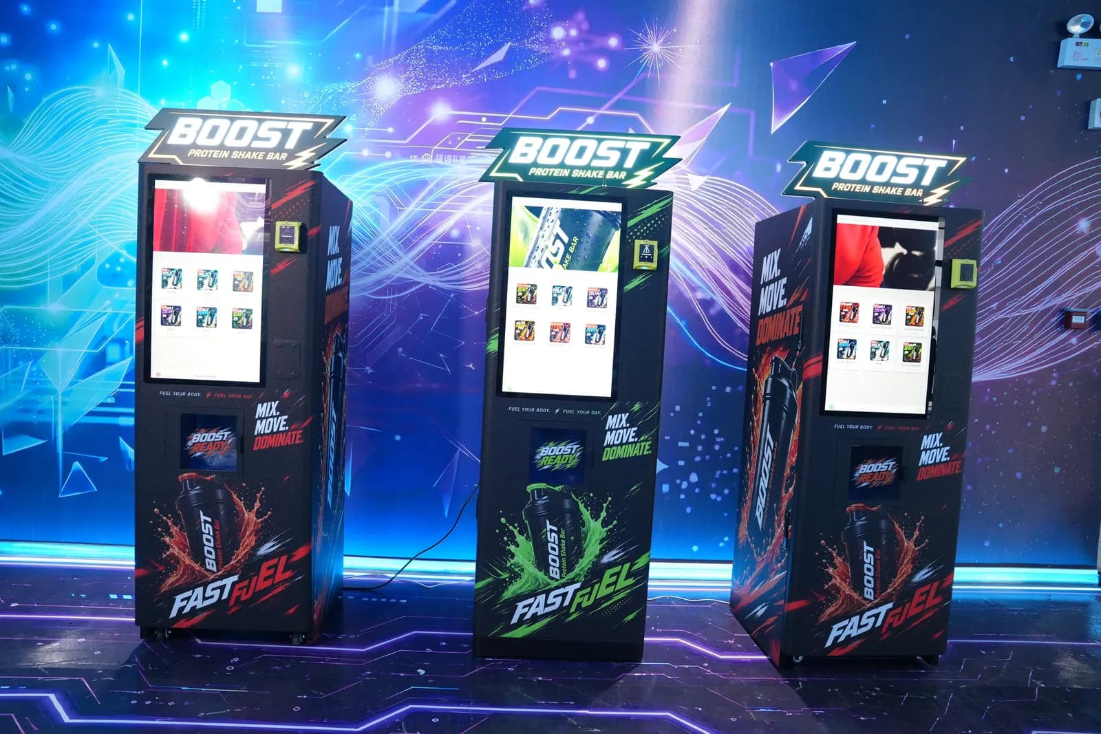 Tres máquinas Boost Protein Shake Bar de Futureino, una junto a otra en el showroom, cada una con su menú en pantalla táctil y el letrero Boost en la parte superior