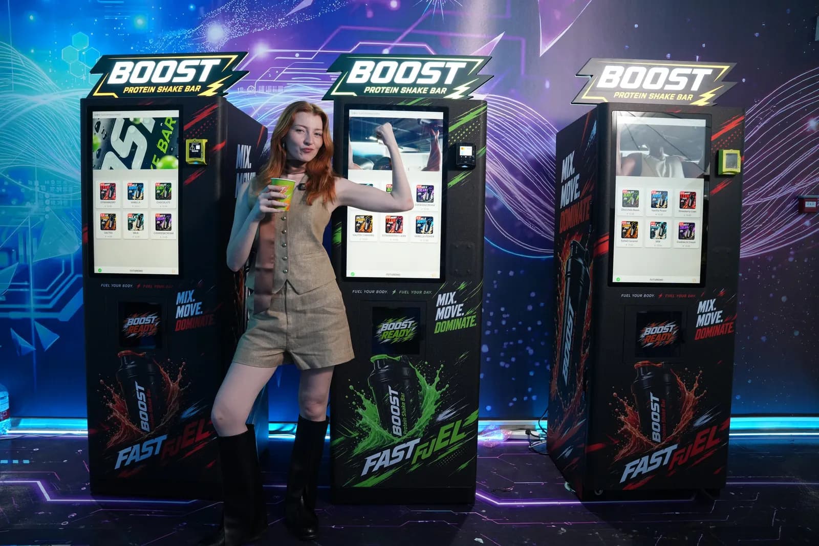 Office worker holding a fresh drink beside three Boost Protein Shake Bar vending machines in the Futureino showroom