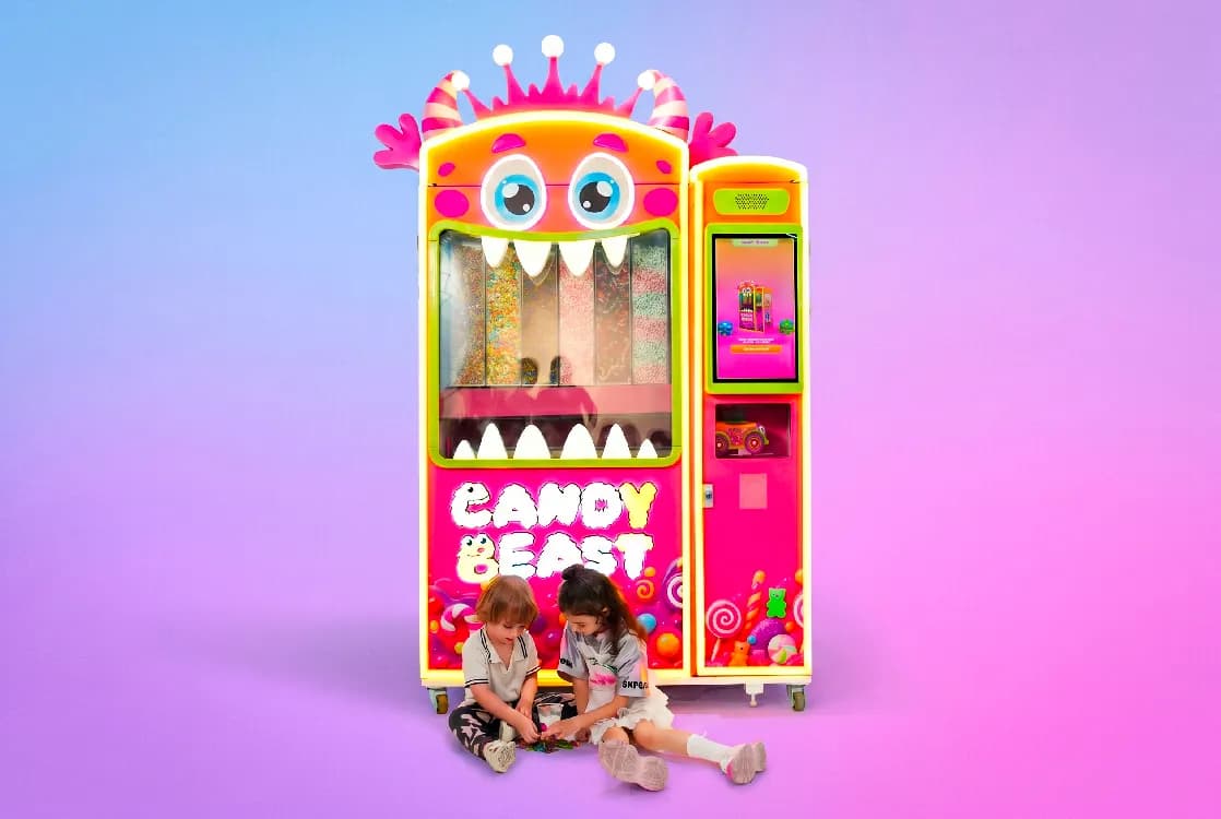 Two kids sitting with candies in front of the Candy Beast machine
