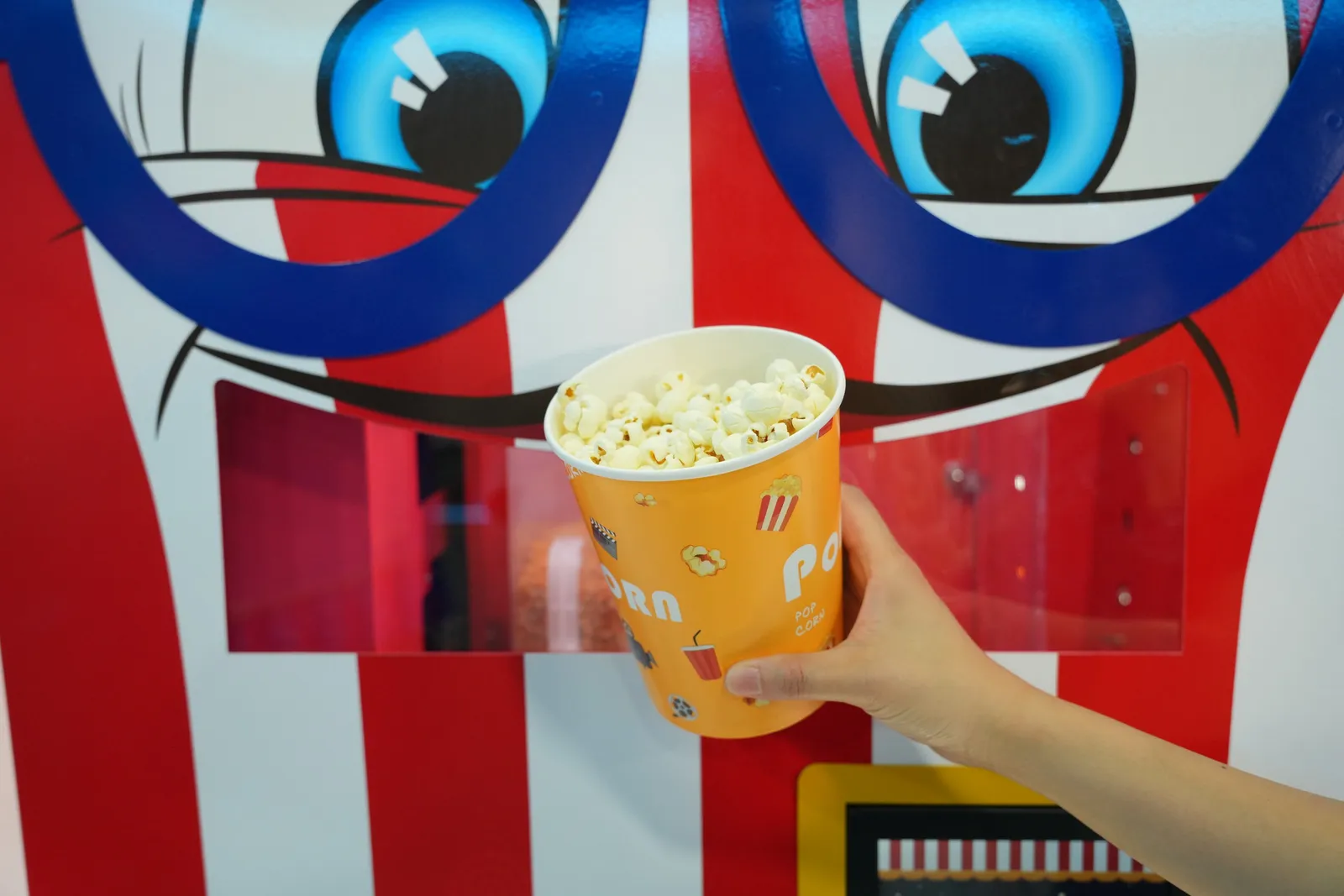 Hand taking a fresh popcorn cup from the Popcorn Bot machine