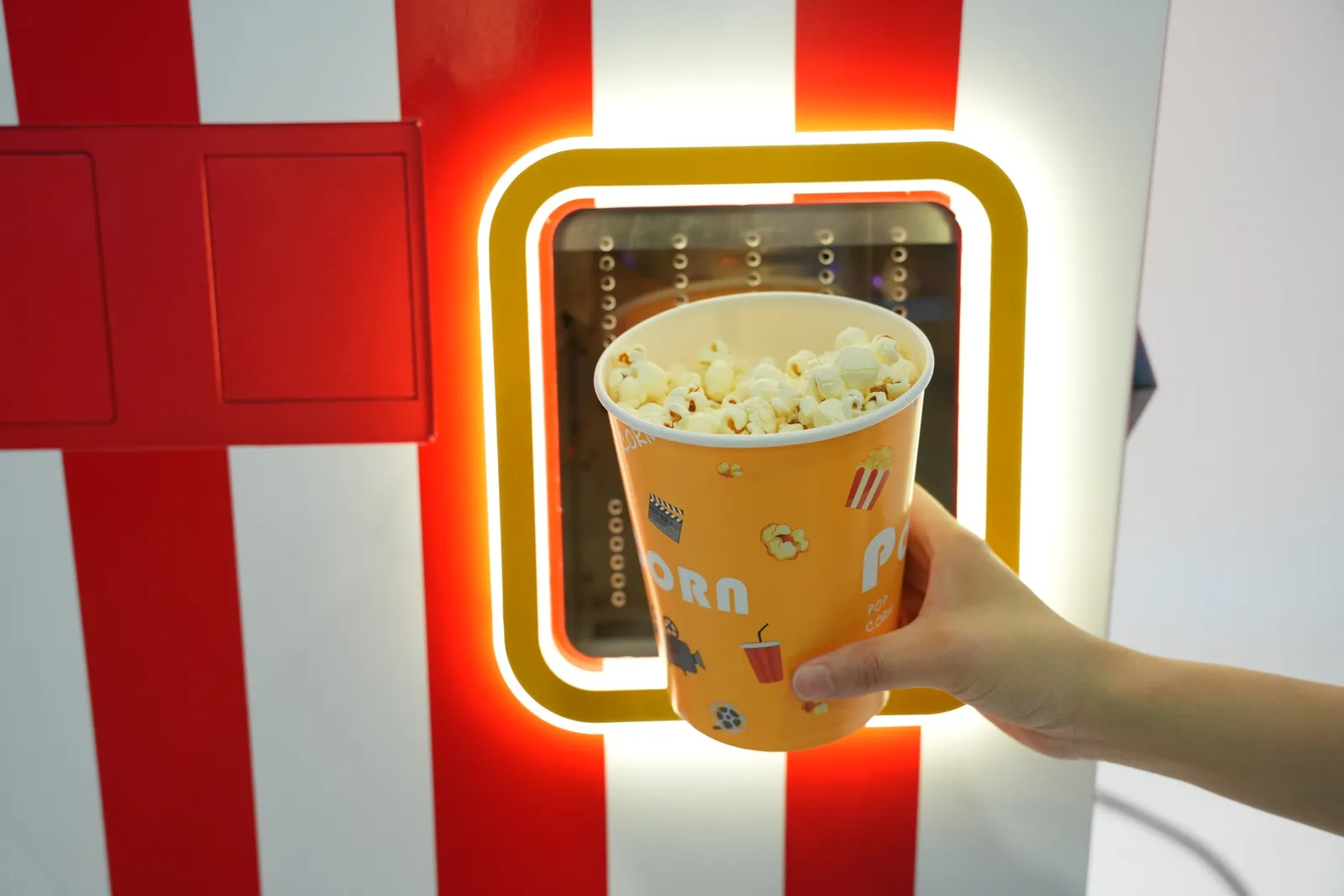 Vaso de palomitas recién hechas recogido en la ventana iluminada de la máquina de palomitas automática de Futureino